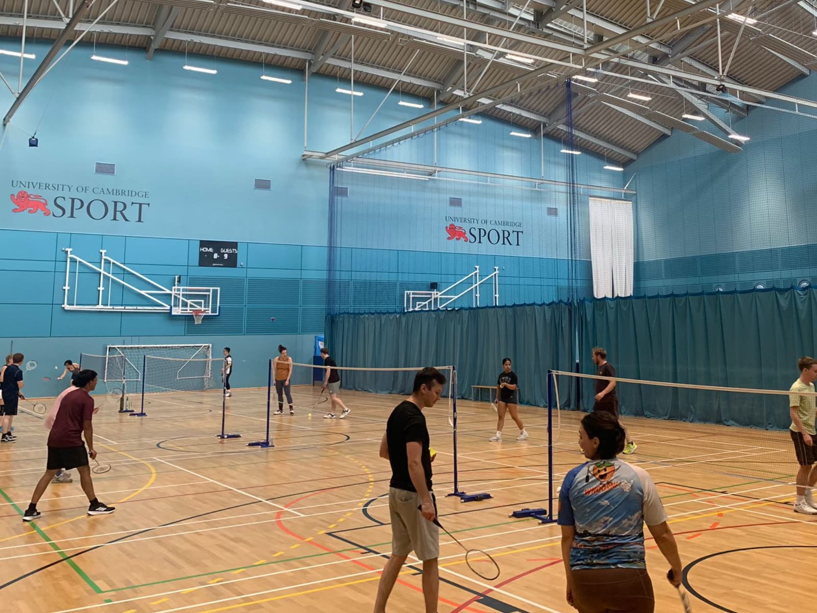 A busy casual badminton session in a sports hall with several courts in play